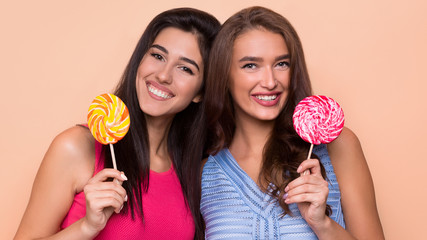 Two attractive fancy friends holding colorful lollipops