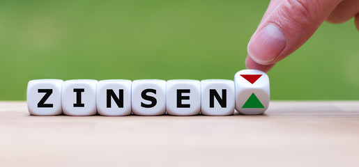 Hand is turning a dice and changes the direction of an arrow symbolizing that the interest rates ("Zinsen" in german) are going up (or vice versa)