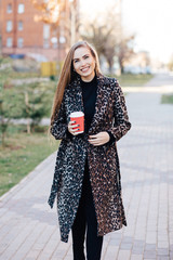 Beautiful stylish woman in the street drinking morning coffee in sunshine light
