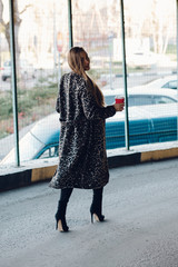 Beautiful stylish woman in the street drinking morning coffee in sunshine light