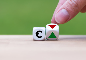 Hand is turning a dice and changes the direction of an arrow symbolizing that the value of the Euro...