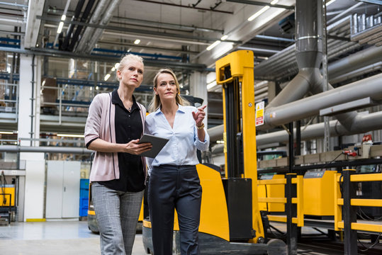 Two women with tablet walking and talking in factory shop floor