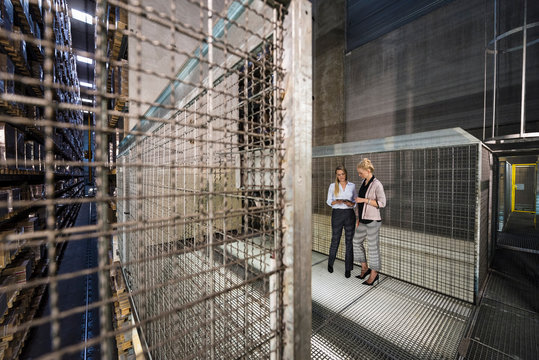 Women using laptop in high rack warehouse