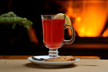 berry tea with lemon in a transparent glass on the background of the fireplace, Christmas tea