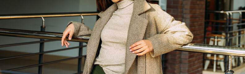 a girl in a beige coat and sweater, a green, long skirt, stands near the railing, leaning on a metal railing. rest, fashion show, challenge.