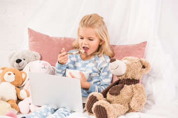 cute child eating cornflakes and watching cartoons in bed