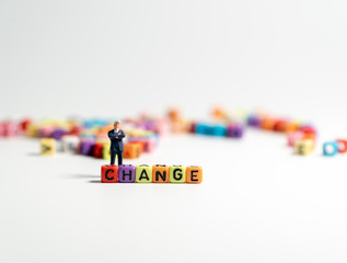 miniature figure businessman in dark blue suit standing backside of colorful of CHANGE alphabet and thinking of the change will come.