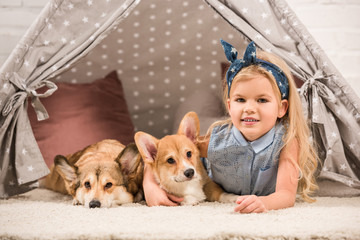 cute child with welsh corgi dogs lying in wigwam and looking at camera © LIGHTFIELD STUDIOS