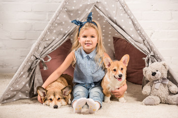 cute child looking at camera and hugging welsh corgi dogs in wigwam at home © LIGHTFIELD STUDIOS
