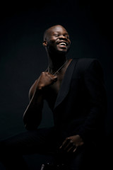 Obraz premium Dark key portrait of handsome smiling male model wearing black jacket and with chainlet on neck. Total black style