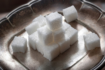 Sugar pieces stacked on a silver saucer, wooden background. Calorie food.