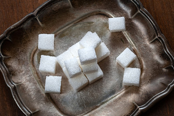 Sugar pieces stacked on a silver saucer, wooden background. Calorie food.