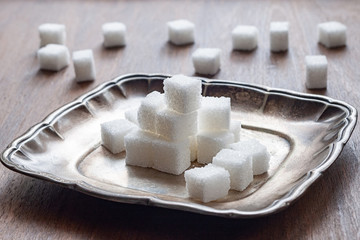 Sugar pieces stacked on a silver saucer, wooden background. Calorie food.