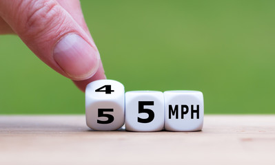 Hand is turning a dice and changes the expression "55 MPH" to "45 MPH" as symbol to reduce the speed limit from 55 to 45 miles per hour