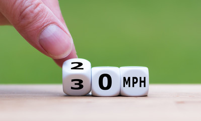 Hand is turning a dice and changes the expression "30 MPH" to "20 MPH" as symbol to reduce the speed limit from 30 to 20 miles per hour