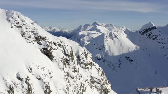 Snowy mountain peaks at winter resort drone view. Aerial view ski elevator, rope way and gazex tube at mountain resort. Drone flying around snowy mountain in valley