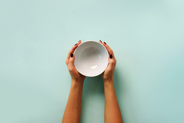 Female hand holding white empty bowl on blue background with copy space. Healthy eating, dieting concept. Banner