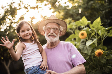 Elderly man with his granddaughter standing between flowers