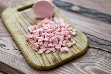Chopped boiled sausage on a wooden board.