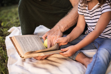 Grandfather with granddaughter reading together in nature