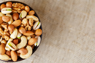 Mix of different nuts in a wooden cup against the background of fabric from burlap. Nuts as structure and background, macro. Top view.