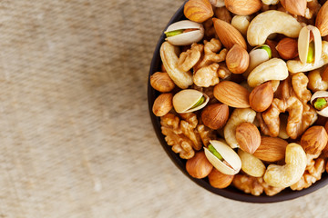 Mix of different nuts in a wooden cup against the background of fabric from burlap. Nuts as structure and background, macro. Top view.