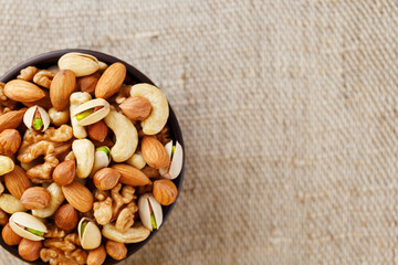 Mix of different nuts in a wooden cup against the background of fabric from burlap. Nuts as structure and background, macro. Top view.