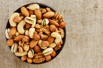 Mix of different nuts in a wooden cup against the background of fabric from burlap. Nuts as structure and background, macro. Top view.