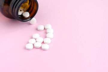 White pills with selective focus in a brown glass bottle on pink background. Antibiotic treatment...