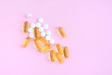 Yellow omega oil capsules with white pills and with selective focus on violet neutral background. Treatment supplements for health care. Vitamin pill and antibiotic. Fish oil gel