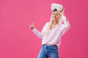 Obraz na płótnie Canvas Young Blond happy woman student with virtual reality goggles. Studio shot on pink background. Virtual learning