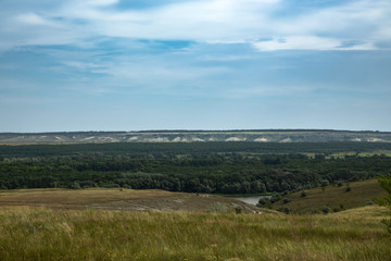 Fototapeta premium View of the forest and fields, chalk mountains from a small elevation on the plain. Beautiful clouds in the blue sky. Summer.