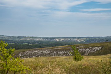 View of the forest and fields, chalk mountains from a small elevation on the plain. Beautiful clouds in the blue sky. Summer.