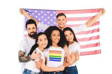 multiethnic group of young people smiling and hugging while holding flag of usa isolated on white