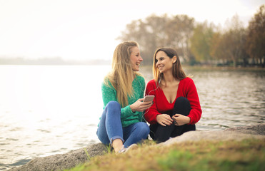 Fototapeta premium Friends listening music with earphones, sitting along the riverside