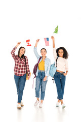 Obraz premium cheerful girls with flags of different countries above heads isolated on white