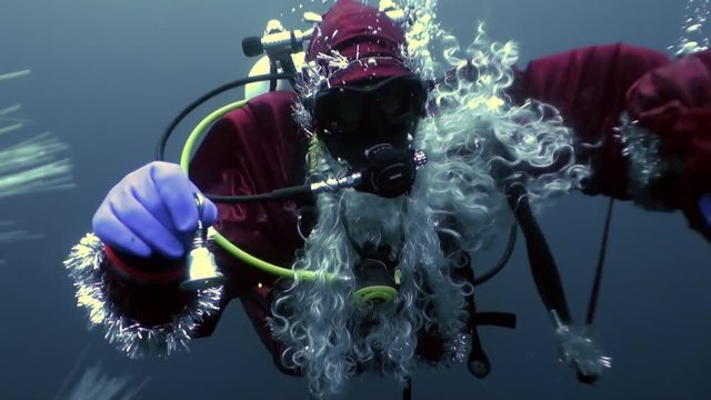 Underwater Santa Claus diver with bell swims in water bubbles in New Year.