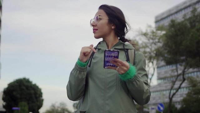 Young attractive Asian female searching for directions. Girl holding her phone and using navigating application to locate herself. Rotating handheld, slow motion footage. Travel concept.
