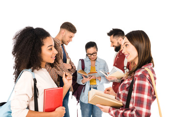 attractive multiethnic girls talking with books in hands near group of young people isolated on white