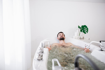Peaceful bearded man enjoying sitting in hydro massage bathtub