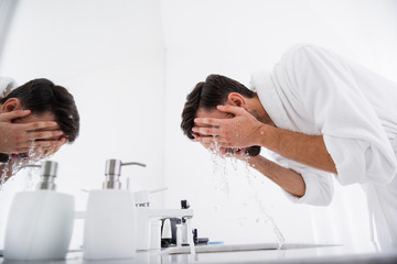 Obraz premium Dark haired man closing his face with hands while washing it