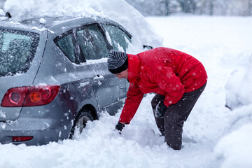 Man is cleaning clean off his car of snow cover by brush. Snow covered car. .