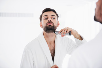 Serious man putting head up while shaving his neck