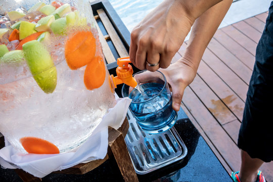 Woman Hands Pulling Down The Lever Of Water Dispenser With Fruit Infused Water