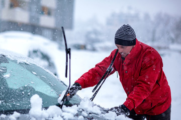 Brush in man’s hand. Man clears snow from icy windshield of car..