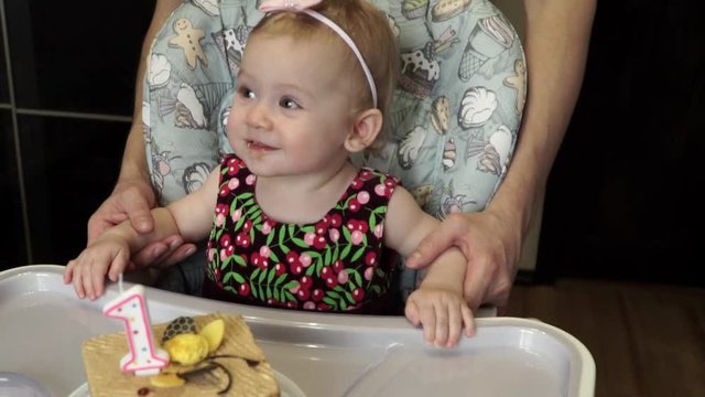 Little cute girl celebrates her anniversary, bites a cake with candles and smiles