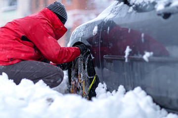 Snow chains on the wheels of car. Man preparing car for travelling at winter day. .