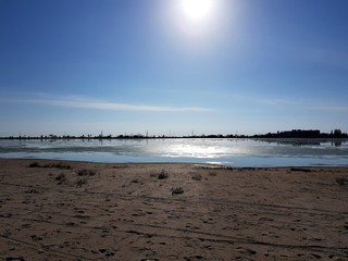 A bright reflection of the sun on the lake. Sand with footprints