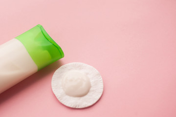 cleansing cream for the face and a cotton pad with a remuver. pink background. makeup removal. skin care. top view. selective focus.