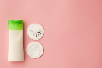 cleansing cream for the face and a cotton pad with a remuver. pink background. makeup removal. skin care. top view. selective focus.
